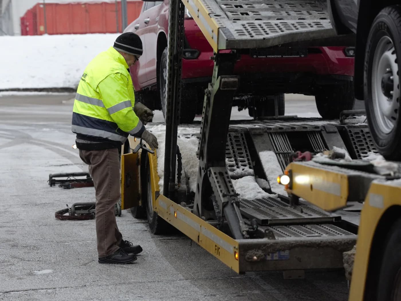 A transport company employee unloading a pickup truck from a car carrier trailer.