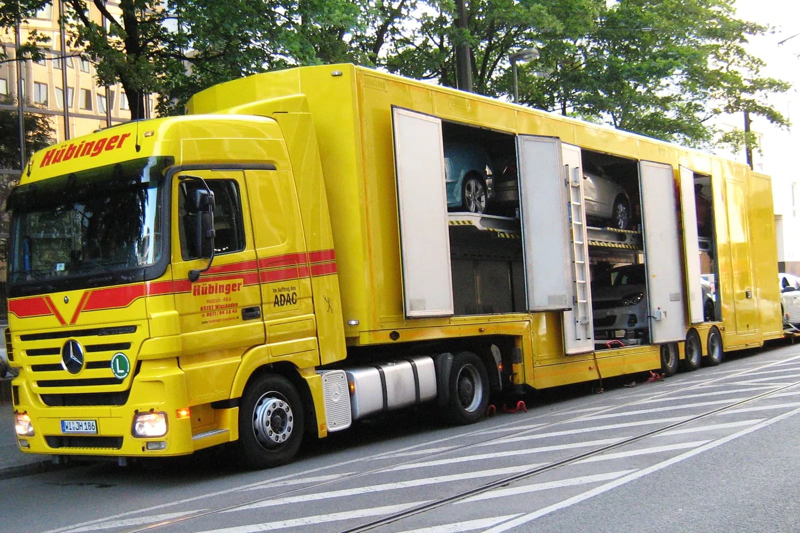 An enclosed multi-deck car transporter trailer behind a yellow Mercedes-Benz tractor unit.