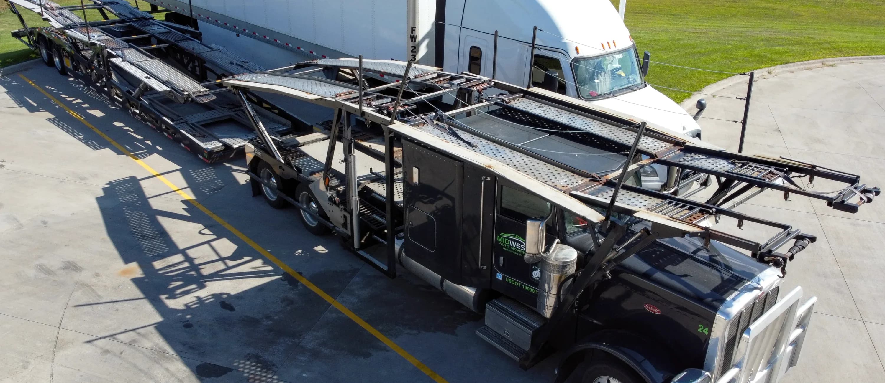 A black truck cab with a car-carrying trailer parked on a paved lot.