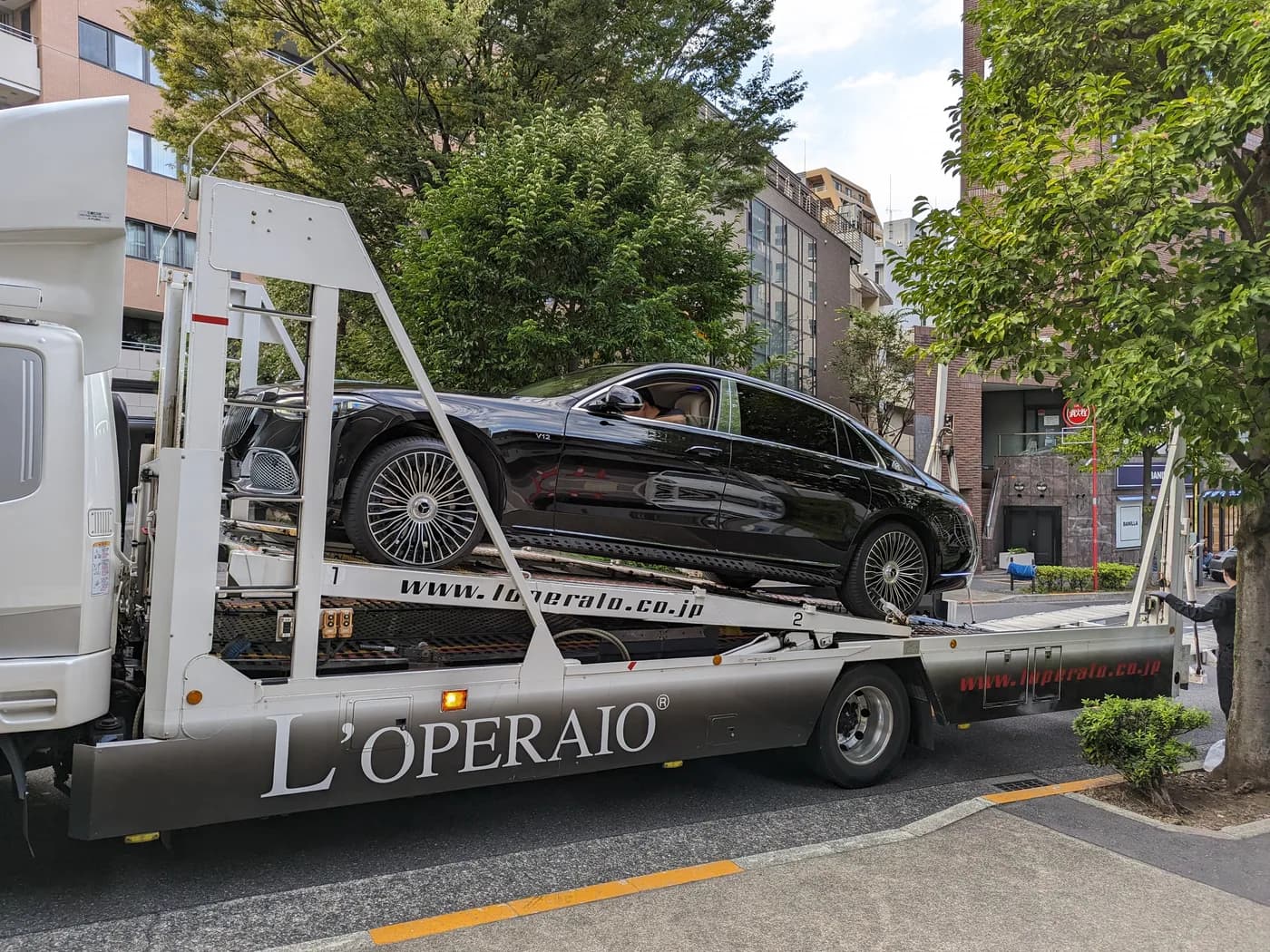 A car sitting on the deck of an open multi-deck car transporter truck parked on a city street.